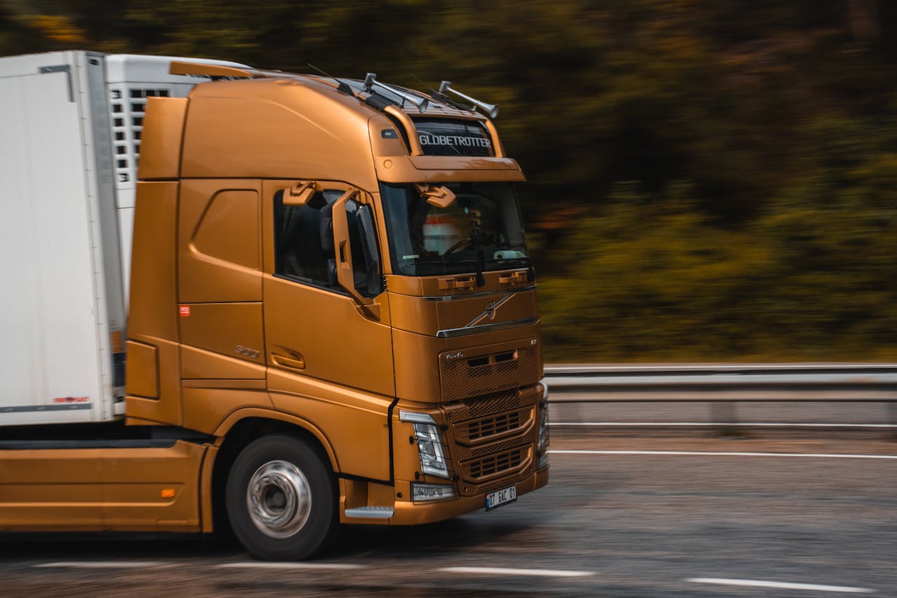 pexels-photo-16706765 Orange truck speeding along a highway in Kemer, showcasing transportation and logistics.